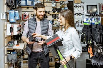 Salesman with young woman buying bicycle pump, paying with card at the sports shop