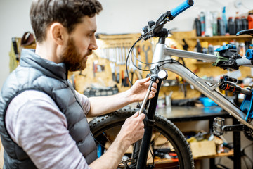 Fototapeta na wymiar Repairman serving a bicycle, checking a air pressure in the pneumatic absorber of a fork in the workshop