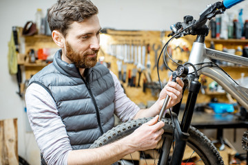 Fototapeta na wymiar Repairman serving a bicycle, checking a air pressure in the pneumatic absorber of a fork in the workshop