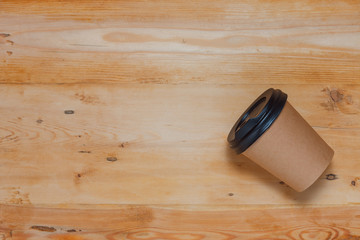 Coffee cup on wooden background and copy space.  Paper cup for drinks with a brown plastic lid. Top view, horizontal position. Place for text. Flat lay.