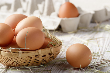 Raw organic brown chicken eggs in square wicker basket on white kitchen wooden table