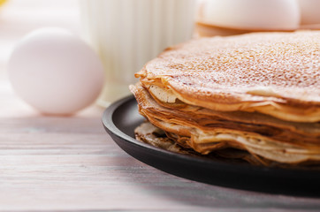 Stack of French crepes in frying pan on wooden kitchen table with milk eggs and flour aside
