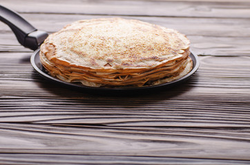Stack of French crepes in frying pan on wooden kitchen table