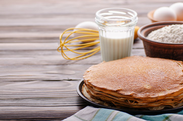 Stack of French crepes in frying pan on wooden kitchen table with milk eggs and flour aside