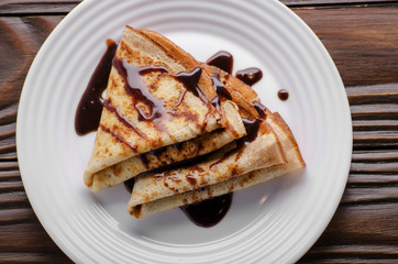 Flat lay French crepes with chocolate sauce in ceramic dish on wooden kitchen table