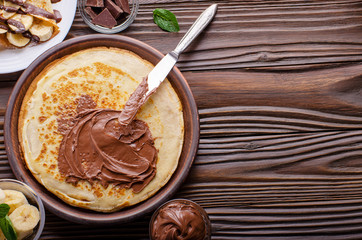 Flat lay French crepes with chocolate sauce and banana in clay bowl on wooden kitchen table