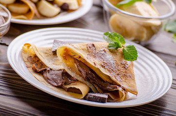 French crepes with chocolate sauce and banana in ceramic dish on wooden kitchen table