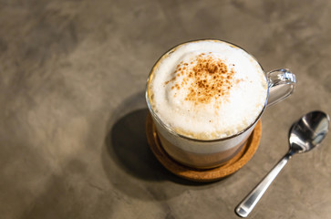 Hot coffee cappuccino with milk foam froth cover on top,sprinkled with chocolate powder or cinnamon,on cement background at coffee shop in the morning