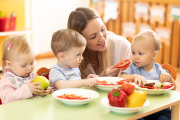 Babysitter feeding nursery babies. Toddlers eat healthy food in daycare center