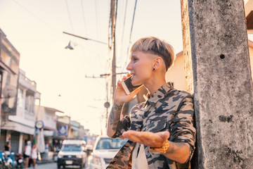 Fototapeta premium Stylish brutal young woman with short hair and shaved temples with a smartphone background of city, rebel and millennial, generation Z