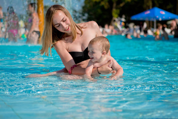 Fototapeta na wymiar Mother and baby in swimming pool. Parent and child swim in a tropical resort. Summer outdoor activity for family with kids. Vacation and traveling with young children. Inflatable toys for water fun