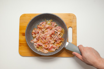 A man holds a frying pan with fried bacon and onions