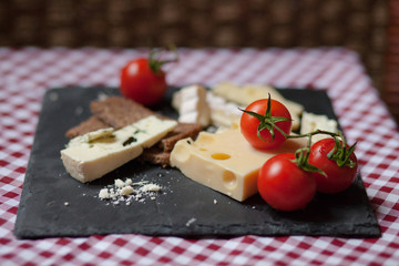 Delicious plate of french cheese served with fresh ripe tomatoes and bread on a black charcoal board. Red and white tablecloth for a picnic mood
