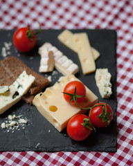 Delicious plate of french cheese served with fresh ripe tomatoes and bread on a black charcoal board. Red and white tablecloth for a picnic mood