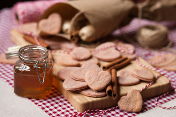 Hand made Saint Valentine's day surprise: home made pink sweet cookies in the shape of heart with a frozen raspberries served on a wooden boar and red napkin. Craft paper cornet on a background