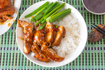 Bowl of rice with teriyaki chicken, chopsticks, cup with sauce on a bamboo napkin, top view. Asian cuisine - Japanese, Chinese, Korean.