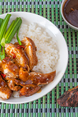 Bowl of rice with teriyaki chicken, chopsticks, cup with sauce on a bamboo napkin, top view close-up. Asian cuisine - Japanese, Chinese, Korean.