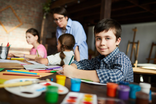Portrait of cute little boy looking at camera while painting pictures in art class, copy space