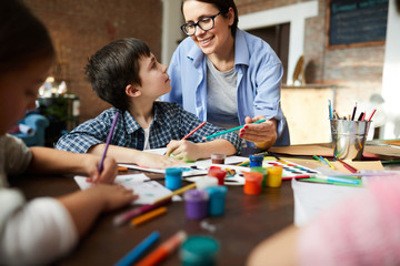 Fototapeta premium Portrait of smiling art teacher working with kids painting pictures in art class, copy space