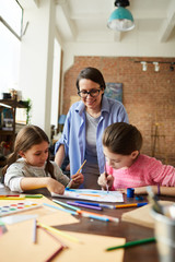 Fototapeta premium Portrait of happy modern mother watching two kids painting at home, copy space