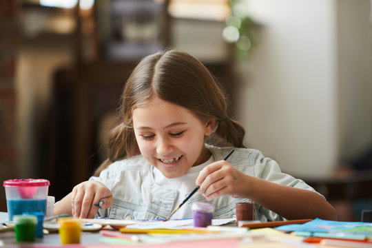 Portrait of cute little girl smiling happily while enjoying painting pictures in art class, copy space