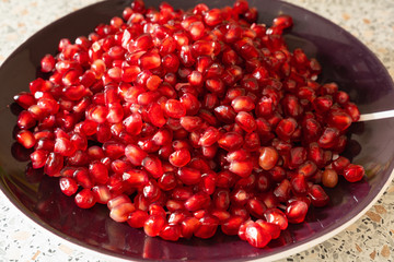 red ripe pomegranate seeds on a plate close-up. the fruit of pomegranate on a table with a marble texture