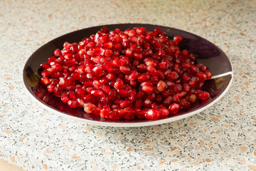 red ripe pomegranate seeds on a plate close-up. the fruit of pomegranate on a table with a marble texture