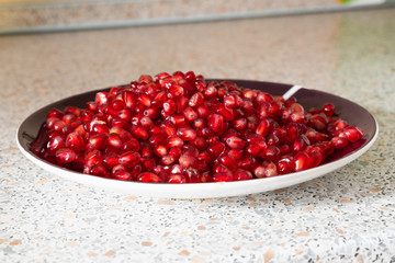red ripe pomegranate seeds on a plate close-up. the fruit of pomegranate on a table with a marble texture