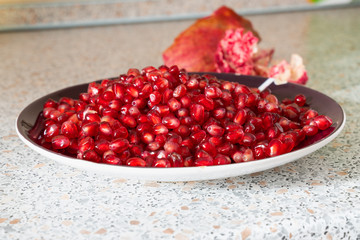 red ripe pomegranate seeds on a plate close-up. the fruit of pomegranate on a table with a marble texture