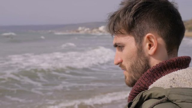 Sad pensive attractive young man contemplatig the sea in a windy day
