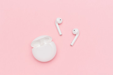 White wireless Bluetooth headphones and charging case on pink paper background.