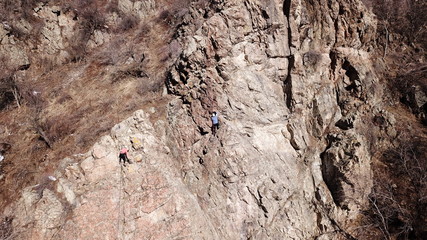 Climbers climb the rock. Drone footage. Side and top view. Rock lesson in the highlands. Gray rocks...