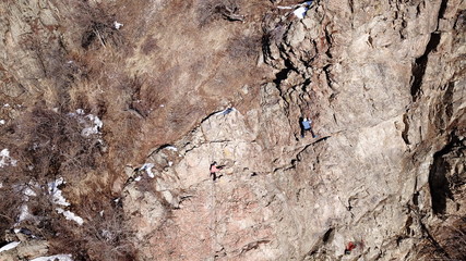 Climbers climb the rock. Drone footage. Side and top view. Rock lesson in the highlands. Gray rocks and dry bushes. Sometimes there is snow. Steep rock and cracks in places.