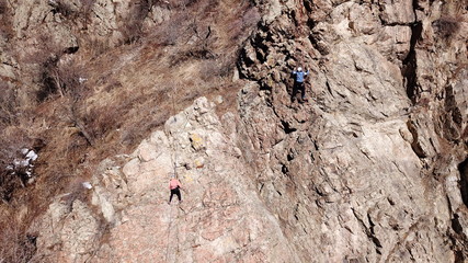 Climbers climb the rock. Drone footage. Side and top view. Rock lesson in the highlands. Gray rocks...