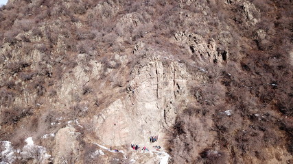 Climbers climb the rock. Drone footage. Side and top view. Rock lesson in the highlands. Gray rocks and dry bushes. Sometimes there is snow. Steep rock and cracks in places.