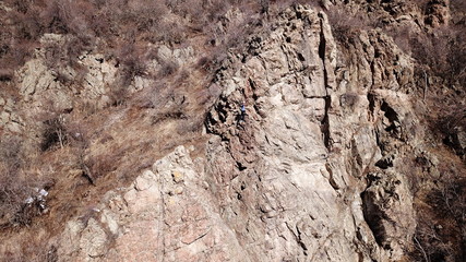 Climbers climb the rock. Drone footage. Side and top view. Rock lesson in the highlands. Gray rocks and dry bushes. Sometimes there is snow. Steep rock and cracks in places.