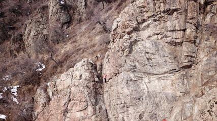 Climbers climb the rock. Drone footage. Side and top view. Rock lesson in the highlands. Gray rocks and dry bushes. Sometimes there is snow. Steep rock and cracks in places.