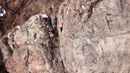 Climbers climb the rock. Drone footage. Side and top view. Rock lesson in the highlands. Gray rocks and dry bushes. Sometimes there is snow. Steep rock and cracks in places.