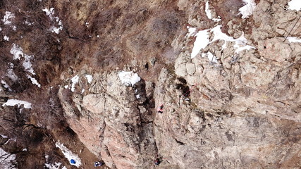 Climbers climb the rock. Drone footage. Side and top view. Rock lesson in the highlands. Gray rocks and dry bushes. Sometimes there is snow. Steep rock and cracks in places.