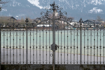 schönes, verziertes, schmiedeeisernes Tor vor dem Wolfgangsee, im Hintergrund Strobl und Blick auf die schneebedeckten Berge © Anita Pravits
