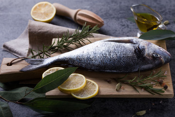 Mediterranean seafood concept. Raw dorado fish with olive oil, lemon, rosemary on stone table. Fresh organic sea bream or dorada fish. Top view dorado fish