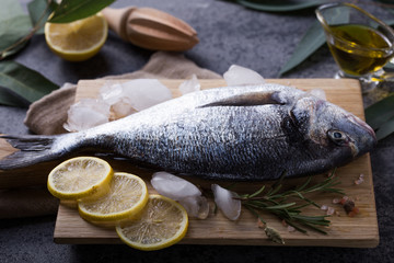 Mediterranean seafood concept. Raw dorado fish with olive oil, lemon, rosemary on stone table. Fresh organic sea bream or dorada fish. Top view dorado fish