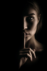 The girl shows a sign of silence. Face on black background, close-up - obrazy, fototapety, plakaty