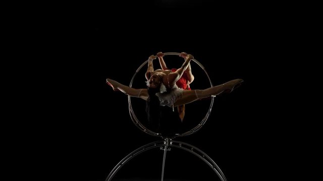 Gymnasts performs a trick in the aerial hoop. Black background