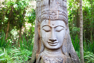 Wooden Buddha head statue with closed eyes on green trees forest background close up