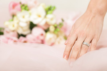 Obraz na płótnie Canvas bride's hand with a wedding ring with diamonds on the background of a bouquet of flowers