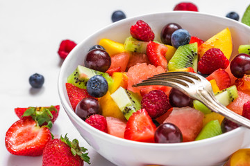 fruit salad with watermelon, strawberry, cherry, blueberry, kiwi, raspberry and peaches in a bowl with fork