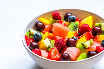 bowl of summer fruit and berry salad on white marble background. healthy vegan food