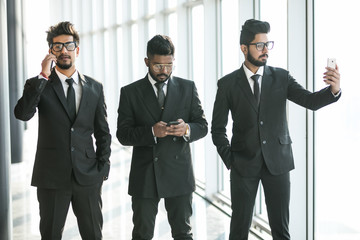 Fototapeta premium Young asian businessmen use phones for call, selfie or typing phone in modern office. Multitask use of phones.