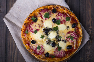Pizza with tomatoes, mozzarella cheese, black olives and basil. Delicious italian pizza on wooden pizza board.